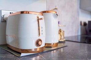 Dos electrodomésticos blancos con detalles en cobre, un enchufe en la pared y una encimera de cocina.