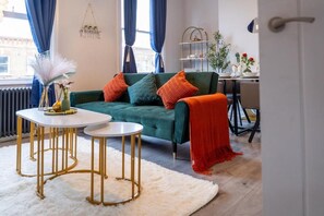 Ein modernes Wohnzimmer mit einem grünen Sofa, weißen runden Tischen und einer roten Decke.