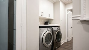 A laundry room with two front-loading washing machines, white cabinets, and a white door. - Brand New - Private Renovated Estate - Secluded! (Brampton)