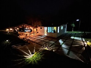 Ett hus med en uteplats, en möblerad, skyddad sittplats och utsikt över staden på natten.