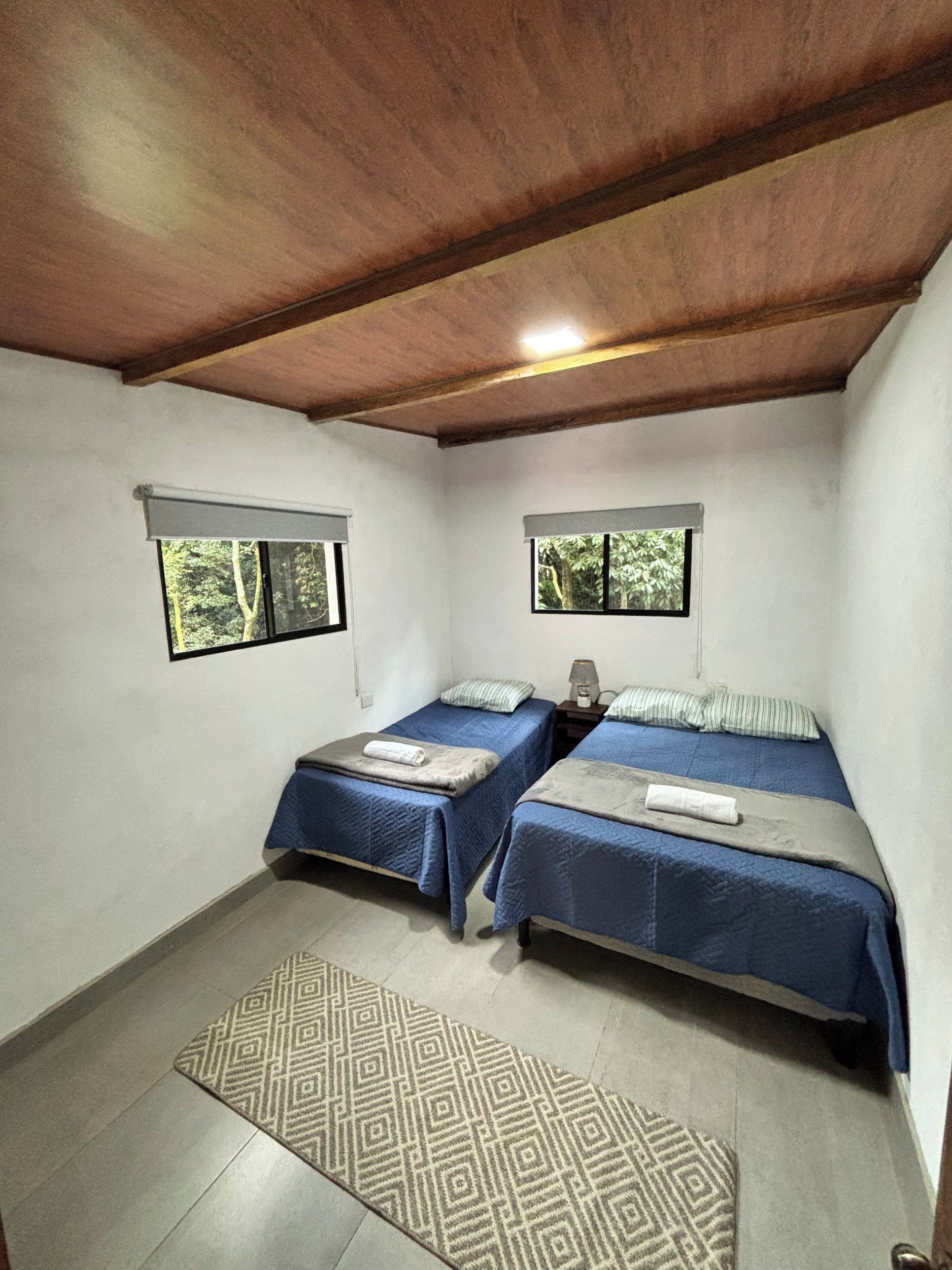 Habitación con dos camas, un tapete estampado y ventanas con vistas al verdor.
