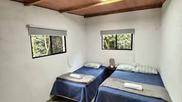 Una habitación con dos camas, un tapete estampado y ventanas que dan a un paisaje de árboles.