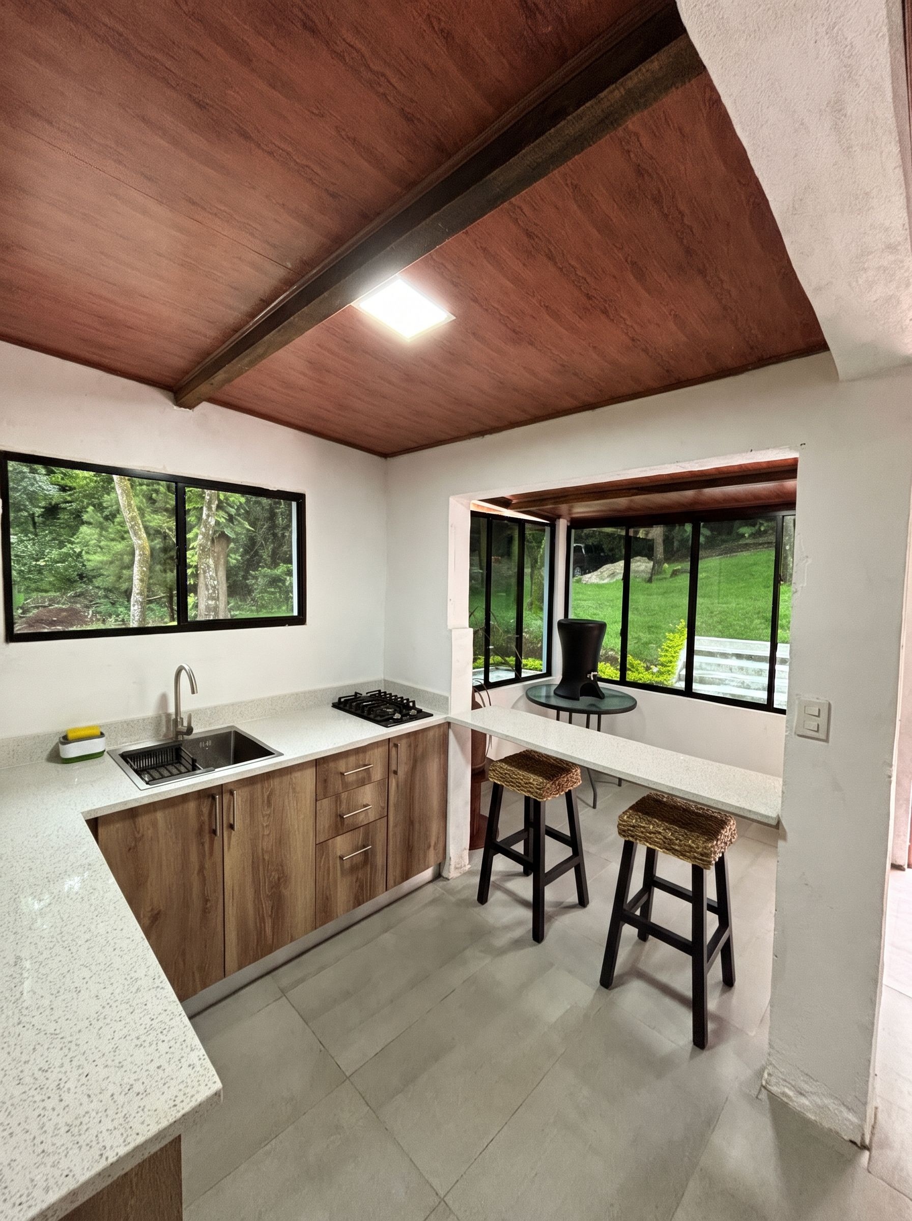 Una cucina con isola centrale, sgabelli da bar, una finestra vista su vegetazione e un soffitto con travi a vista.