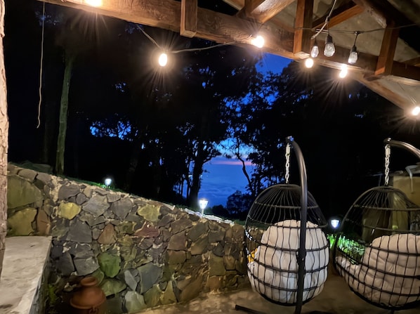 A stone wall, hanging chairs, and string lights.