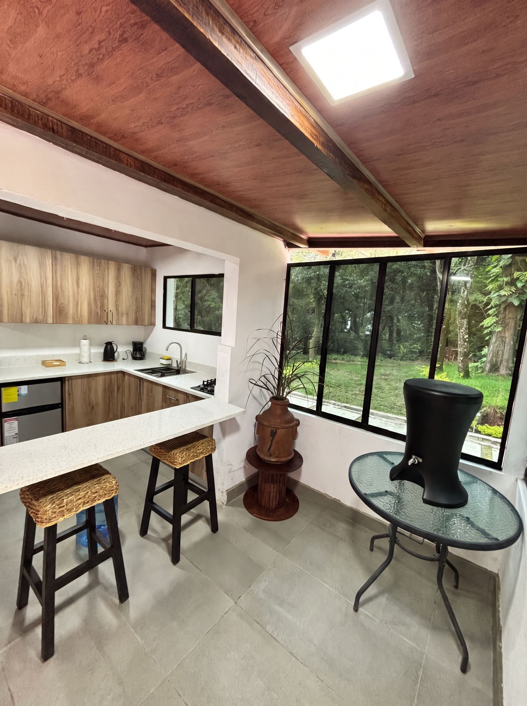 A modern kitchen with a large window, a bar stool, and a potted plant.