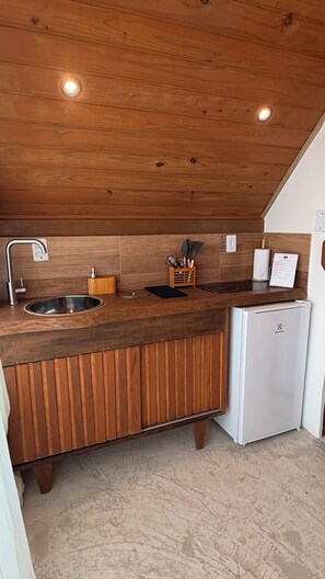 A kitchen with wooden cabinetry, a stainless steel sink, and a white refrigerator. - Chalés do Alto Boutique (Angra dos Reis)