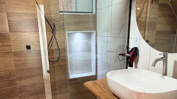 A modern bathroom with a glass shower enclosure, a white sink, and a wooden vanity.