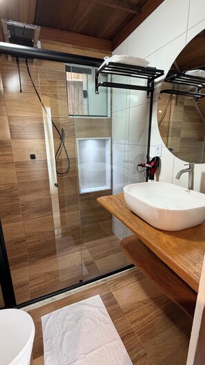 Un baño moderno con cabina de ducha de vidrio, un lavabo blanco y un mueble de tocador de madera.