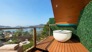 A hot tub on a wooden deck with a view of the sea and hills.
