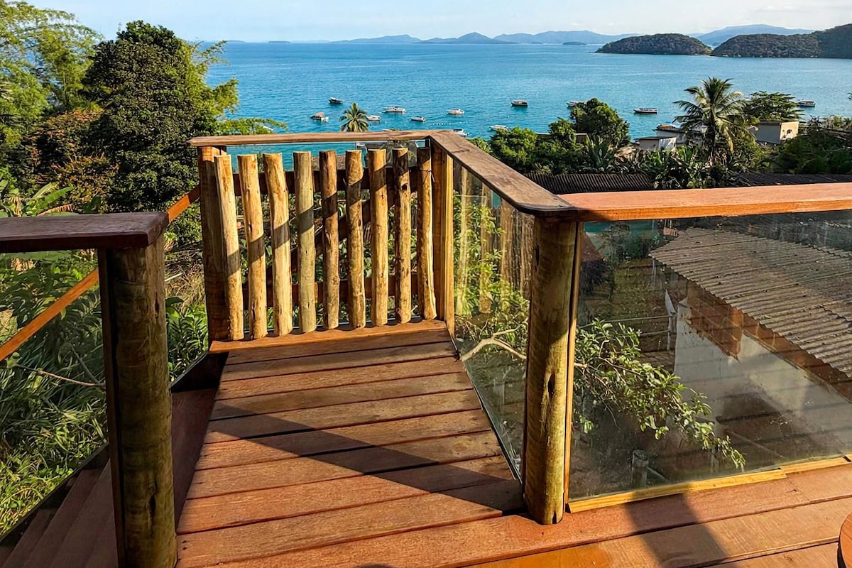 A wooden deck with a glass balustrade overlooking a coastal view with boats and distant land.