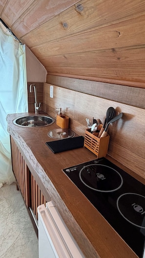 Una cocina compacta con un lavamanos, grifo, encimera de madera y una placa de inducción integrada.