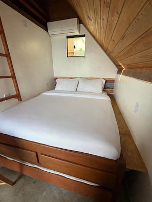 A single bed with a wooden frame and white bedding in a room with a sloped ceiling and wooden paneling. - Chalés do Alto Boutique (Angra dos Reis)