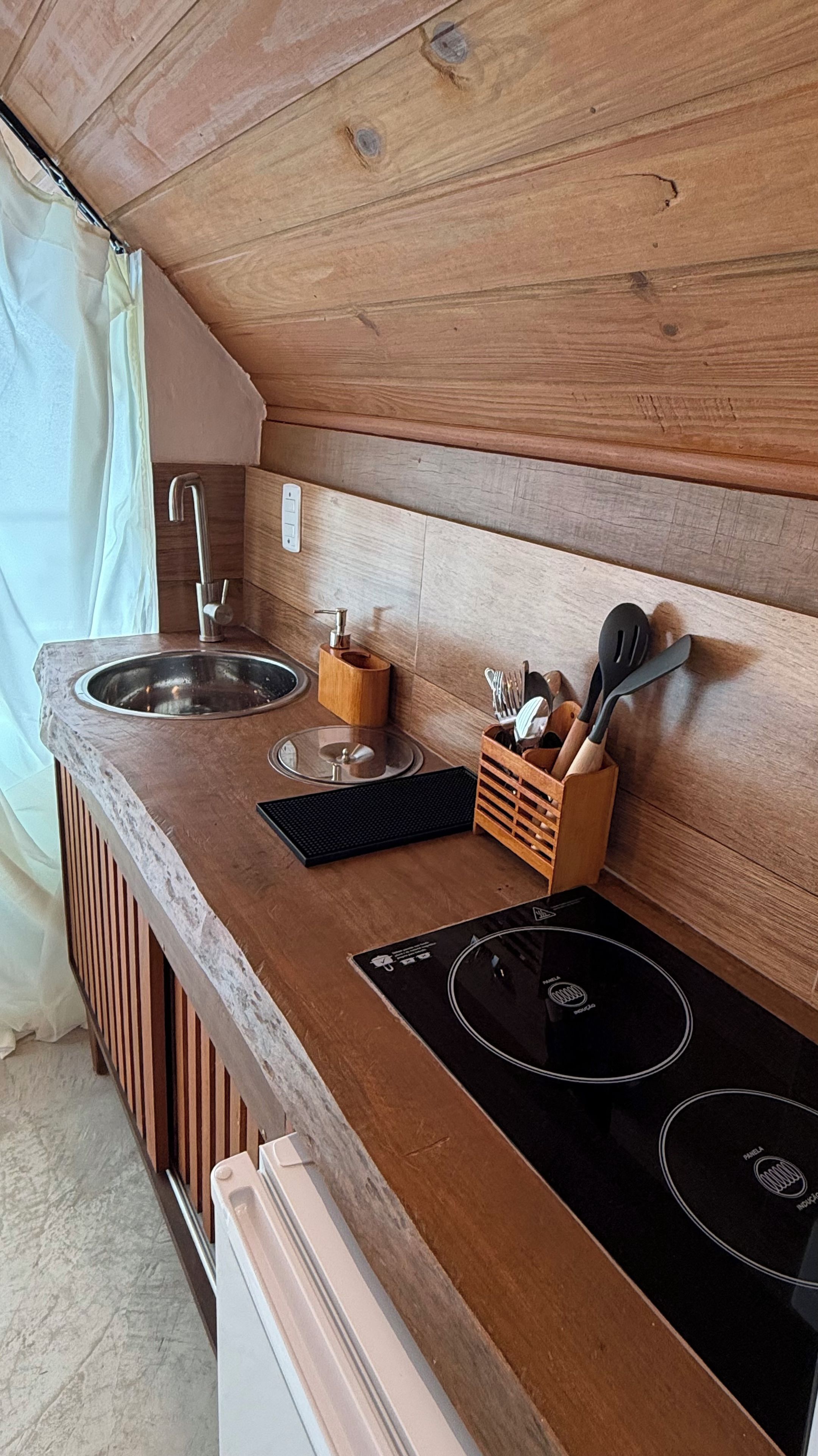 A compact kitchen with a sink, faucet, wooden countertop, and a built-in induction cooktop.