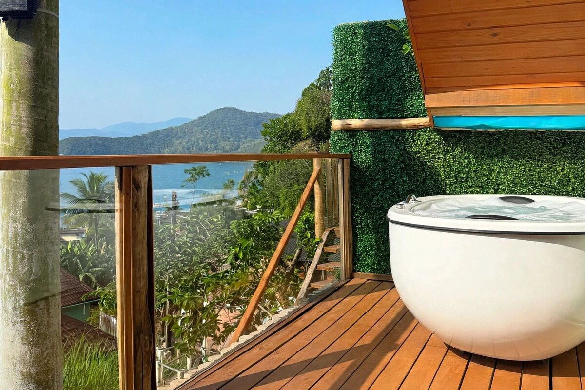 A wooden deck with a hot tub, a glass balustrade, and a view of a coastal landscape.