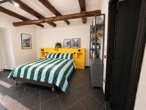 Una camera da letto con un letto, una testiera gialla, un armadio grigio e una porta nera.