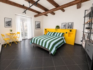 Una camera con un letto, una scrivania, sedie, una finestra con tende e una parete decorata con quadri.