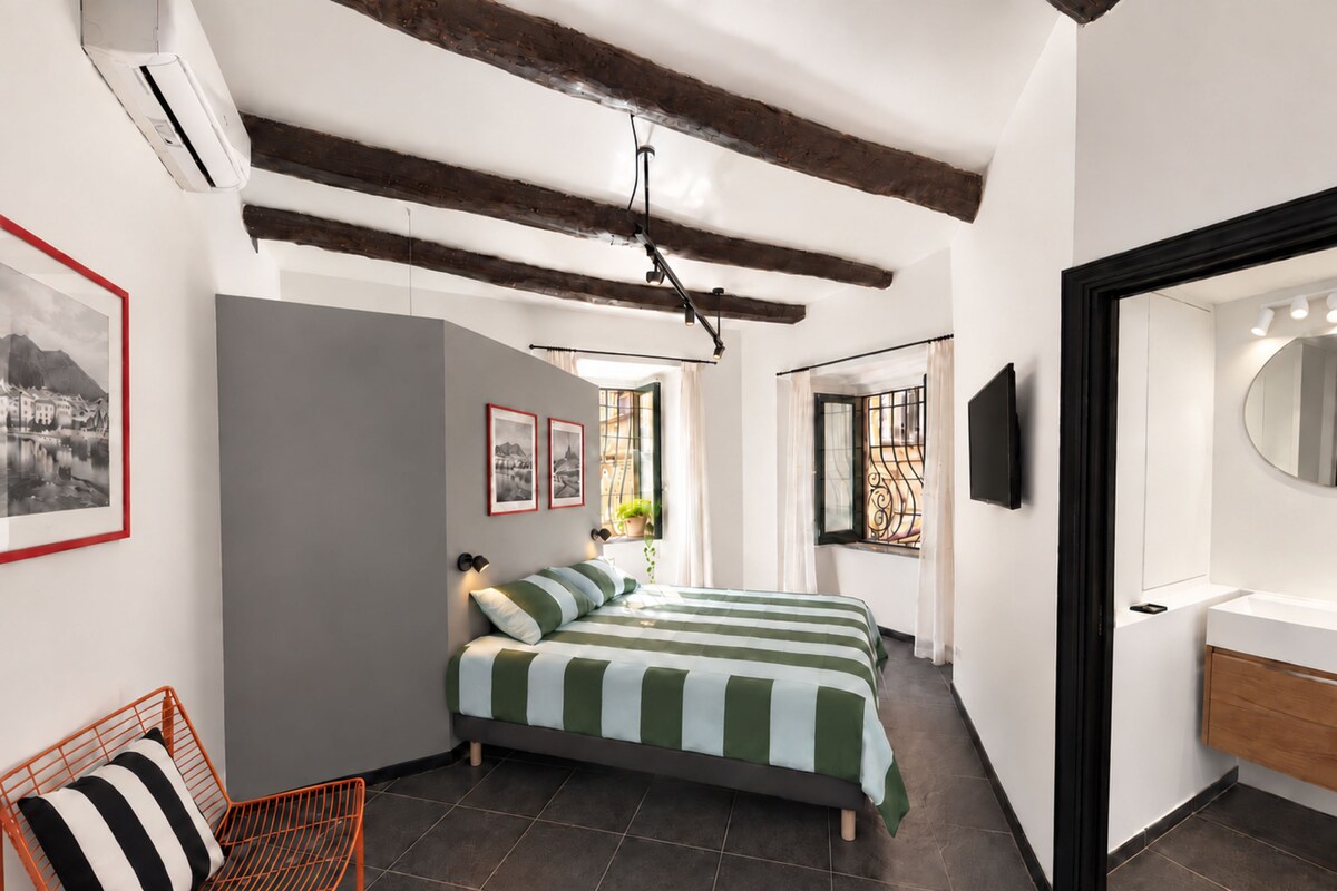 Una camera da letto con un letto, una sedia, una TV e un bagno con uno specchio.