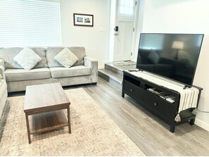 A living room with a sofa, a coffee table, a TV stand, and a flat-screen TV. - Sunset Stay, Pet friendly (Boise)