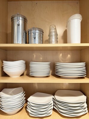 A wooden shelf with metal containers and stacks of white plates.