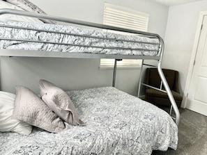 A bunk bed with patterned bedding, a chair, and a door in a room with plain walls.