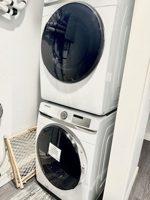 A stacked washer and dryer unit with a control panel and a label indicating 'Please leave washing machine door open after use.'
