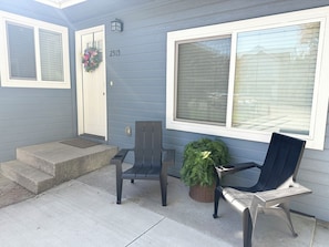 A front porch with two chairs, a potted plant, and a door with a wreath.