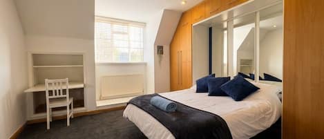 A bedroom with a bed, a desk, and a window.