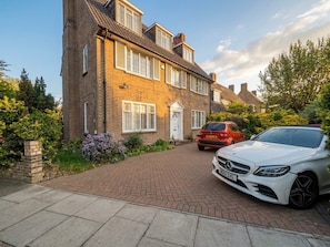 A two-story brick house with a driveway leading to a white car parked on the right. - Lovely-bedroom house in London perfect for your city escape (London)