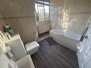 Une salle de bain avec une baignoire, des toilettes, une fenêtre et un radiateur.
