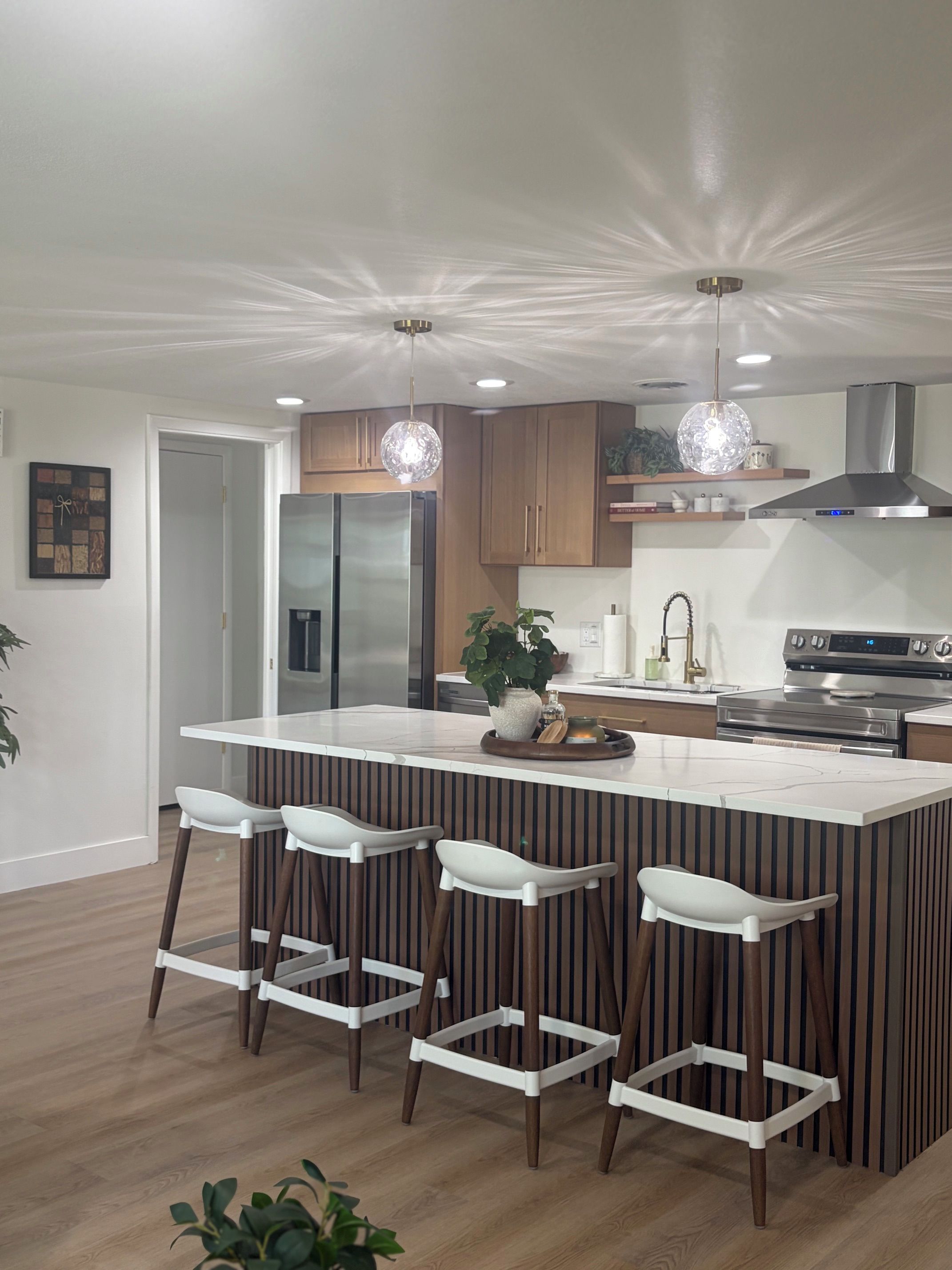 A modern kitchen with a central island, bar stools, stainless steel appliances, and pendant lighting.