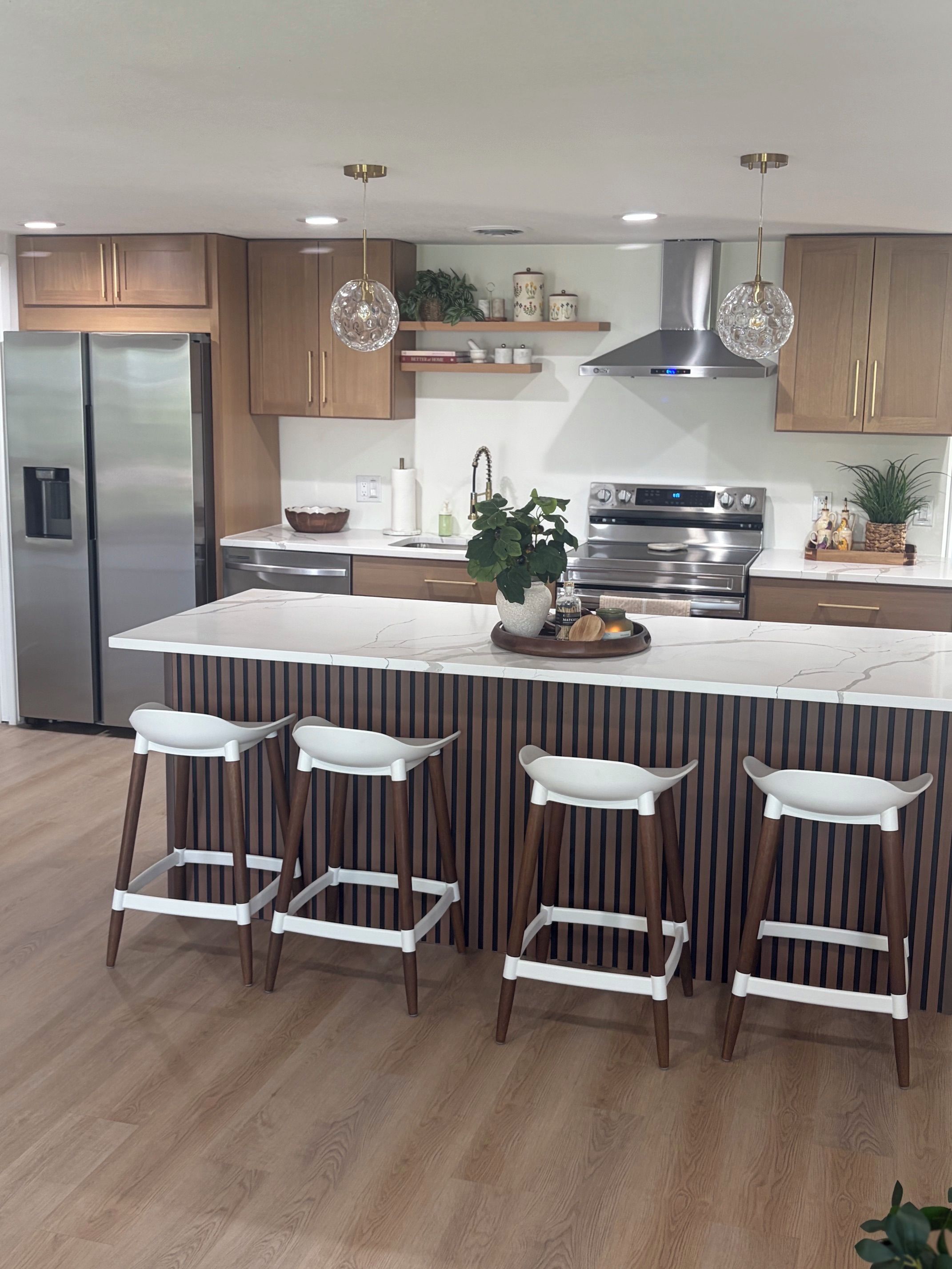 A modern kitchen with a central island, bar stools, stainless steel appliances, and wooden cabinetry.