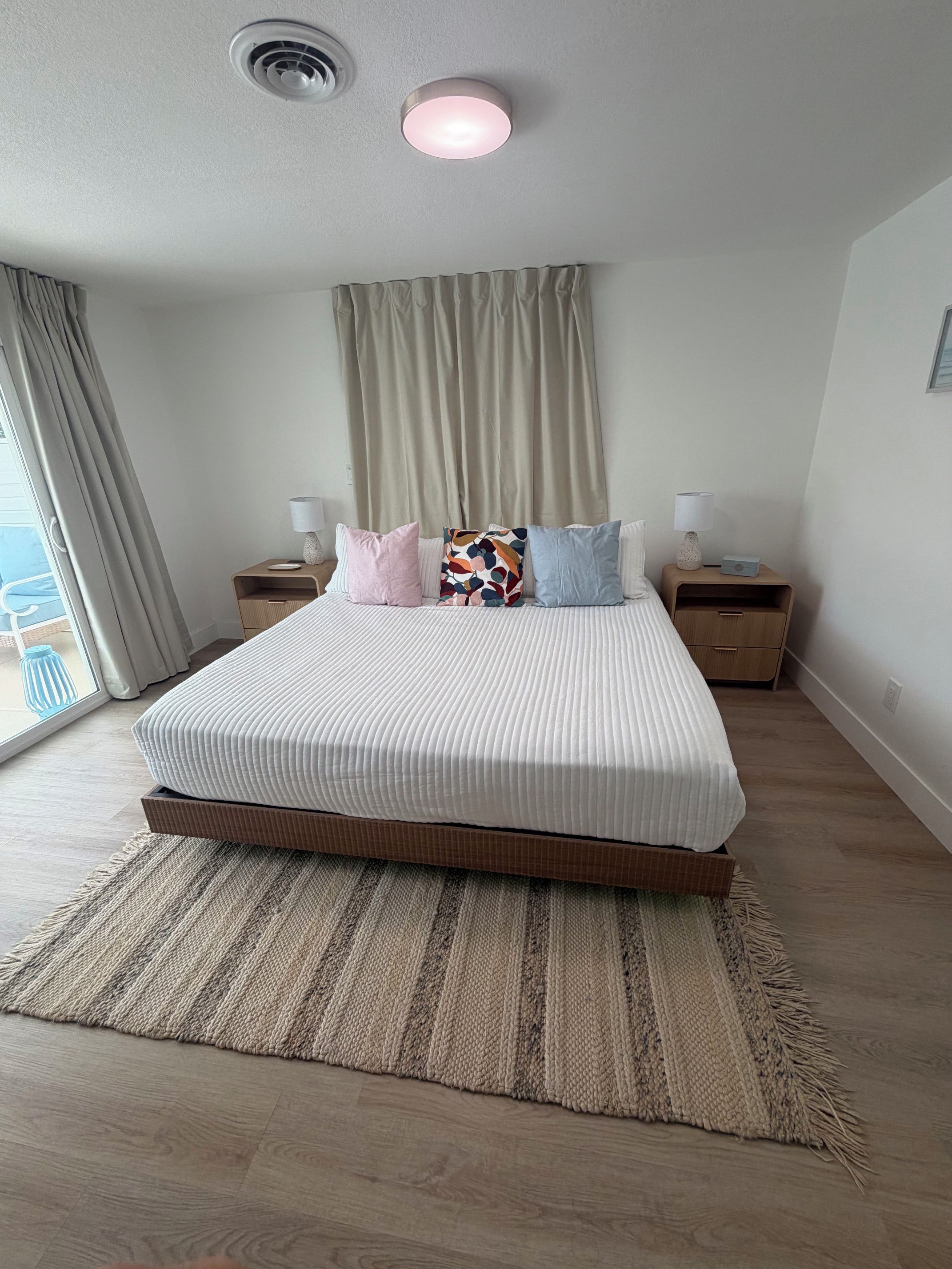 A modern bedroom with a large bed, two bedside tables, a ceiling light, and a view through a window.