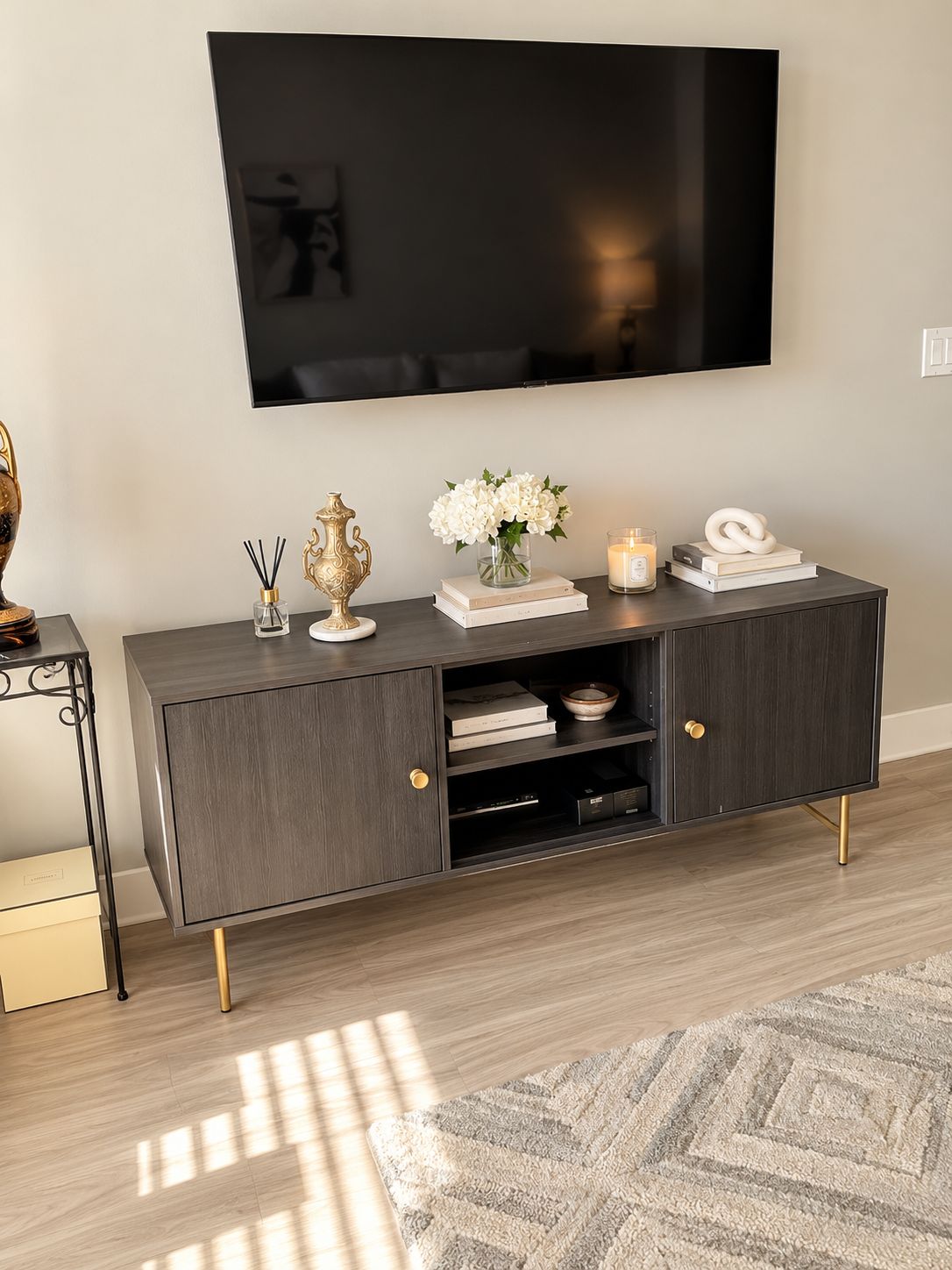 Un salon moderne avec une console en bois foncé, un téléviseur à écran plat fixé au mur et un tapis à motifs sur le sol.