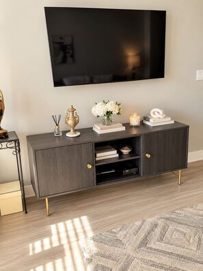 Een moderne woonkamer met een donkerhouten salontafel, een flatscreen televisie aan de muur en een vloerkleed met dessin.