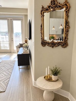 A hallway with a round table, a decorative mirror, and a view into a kitchen area.