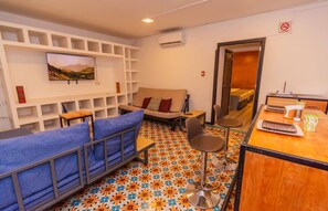 A hotel room with a sofa, chairs, a TV, a small table, and a bed. - Humboldt | Loft with AC in the Historic District (Oaxaca de Juárez)