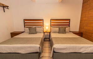 Ett hotellrum med två separata sängar, sänggavlar i trä, sängbord och en accentvägg i tegel.