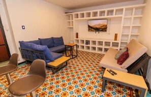 A room with a sofa, chairs, a small table, a TV on a wall, and a patterned floor. - Humboldt | Loft with AC in the Historic District (Oaxaca de Juárez)