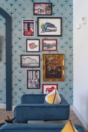A wall with a series of framed pictures and a blue sofa with a cushion. - Bright and Modern Retreat Near UGA & Five Points (Athens)