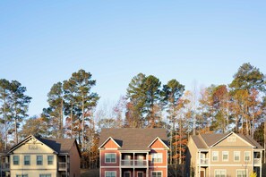 A row of two-story residential buildings with a central balcony, surrounded by tall trees and a clear sky. - Bright and Modern Retreat Near UGA & Five Points (Athens)