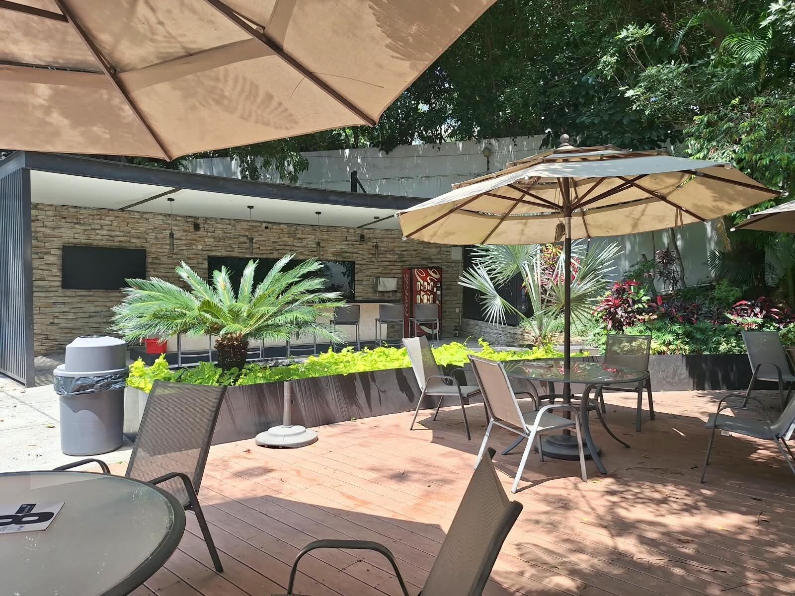 An outdoor patio area with tables and chairs, a large umbrella, and a stone wall with greenery.
