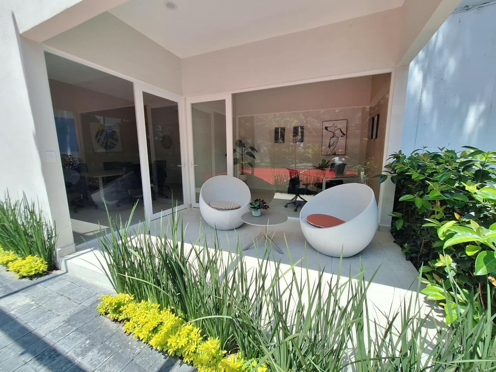 A modern outdoor seating area with two white chairs, a glass door leading to an interior space, and a small table.