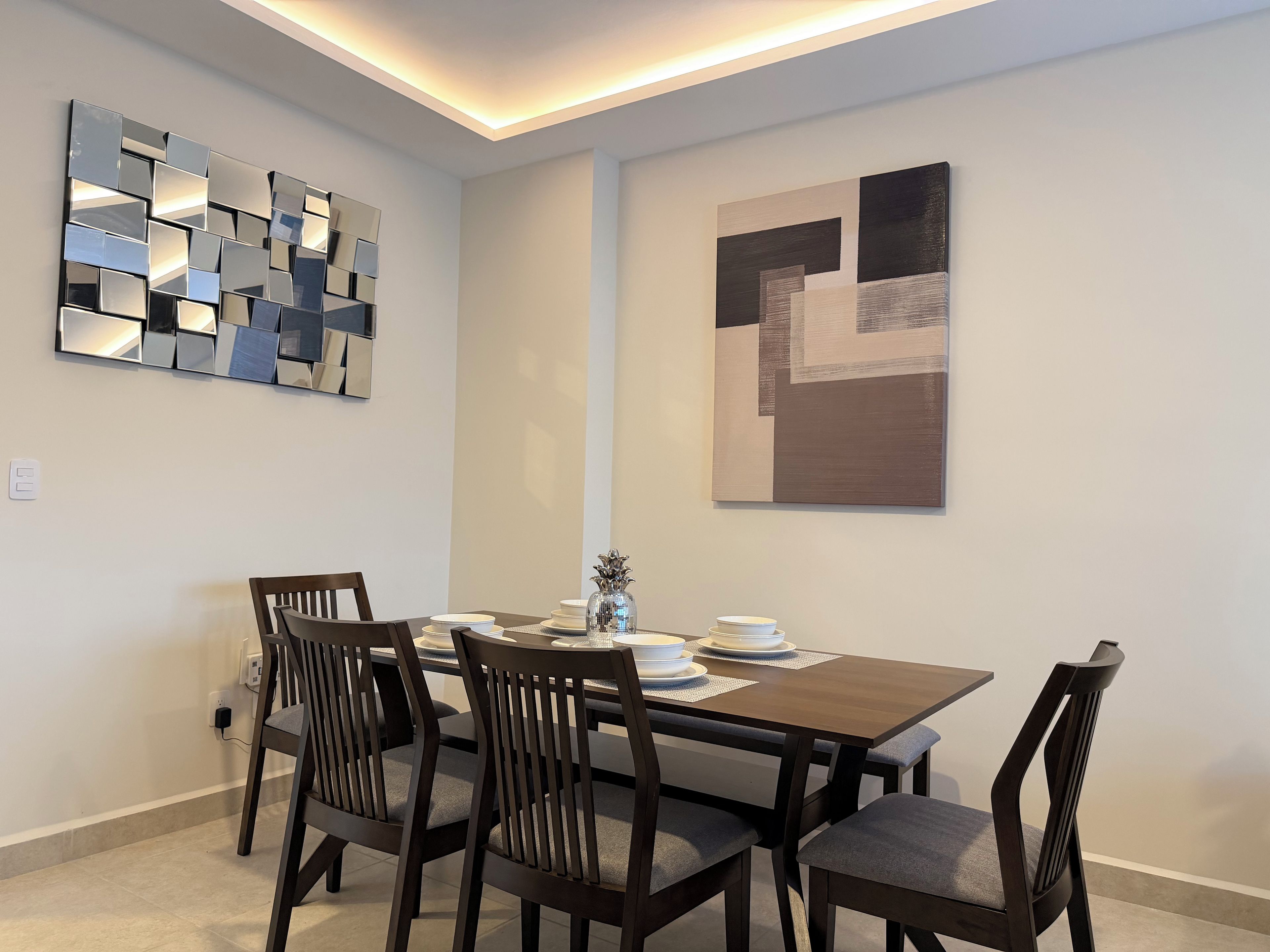 A dining area with a rectangular table, four chairs, and two wall-mounted abstract art pieces.