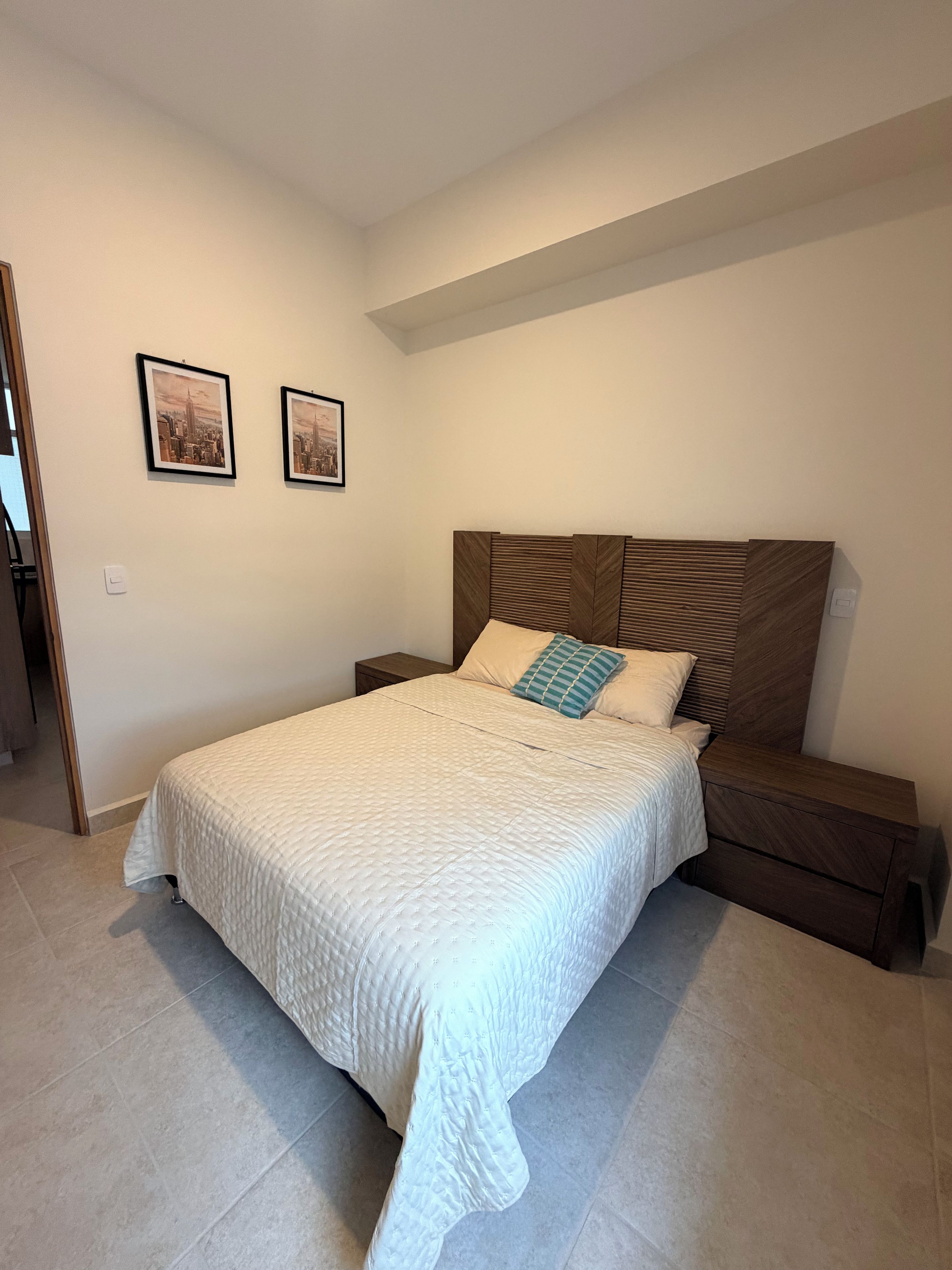 A bedroom with a bed, a nightstand, and two framed pictures on the wall.