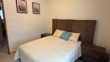 A bedroom with a bed, a nightstand, and two framed pictures on the wall.