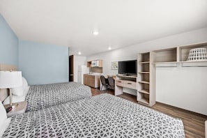 A hotel room with two beds, a desk, a television, and built-in shelving.