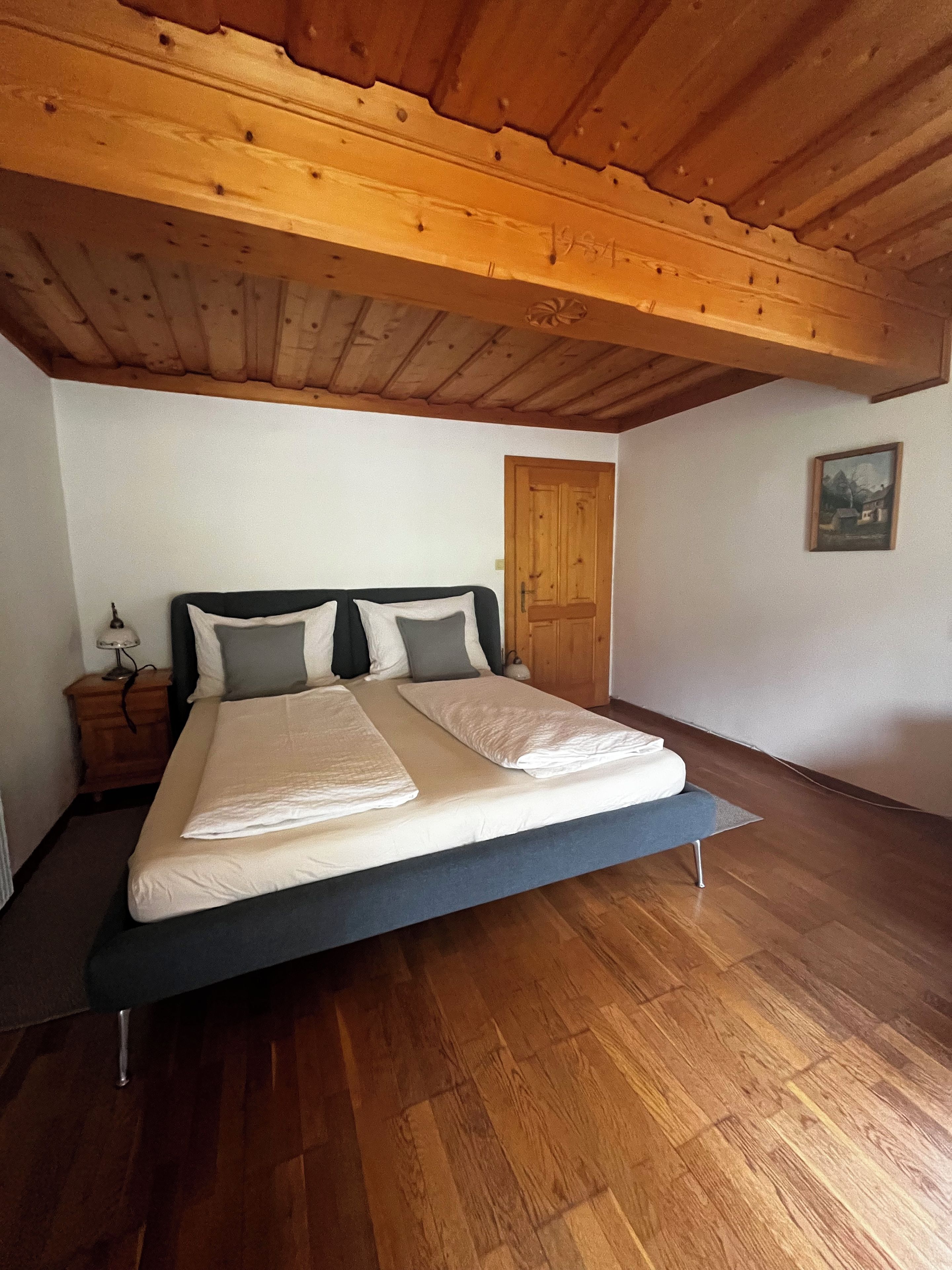 Ein Schlafzimmer mit Holzbalkendecke, einem Bett mit weißer Bettwäsche, einem Nachttisch und Holzboden.