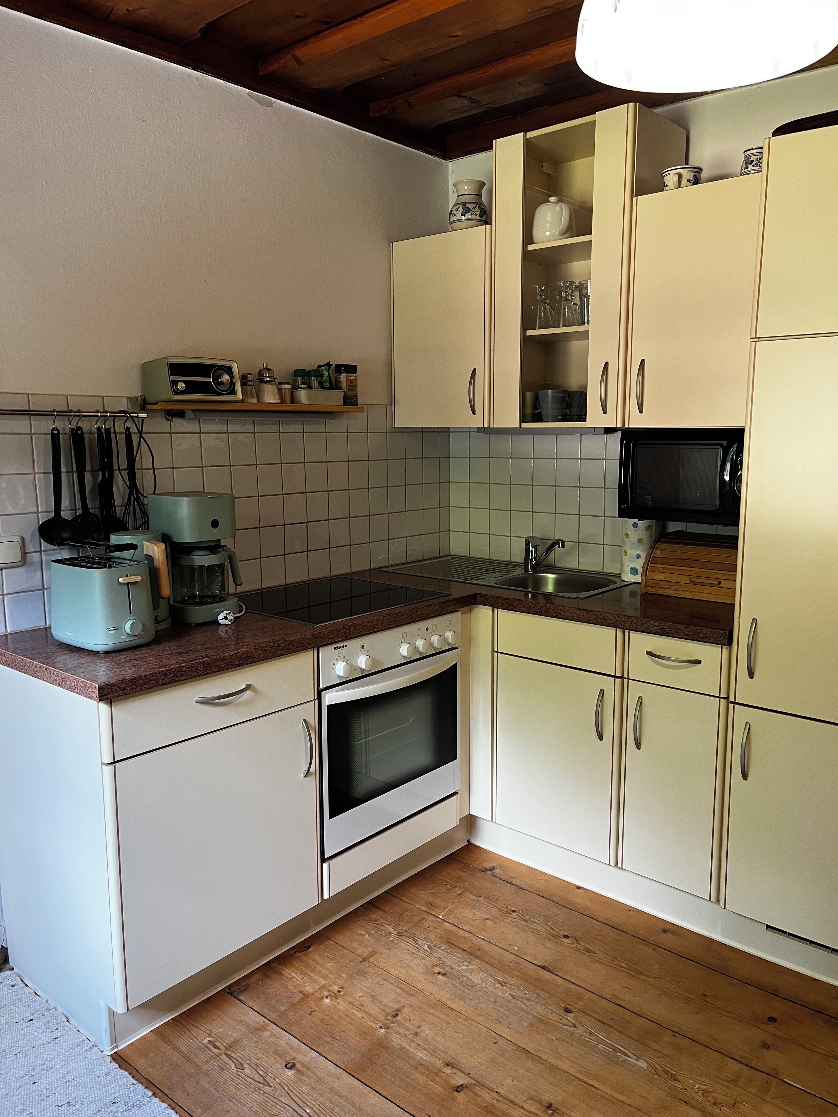 Una cocina con gabinetes blancos, microondas, estufa y cafetera.