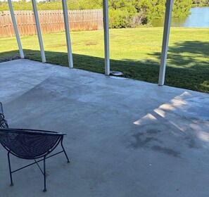 A covered patio area with a concrete floor, a metal chair, and a wooden fence in the background. - Florida Farm House, Beaches, Boating, Fishing, Shopping, Restaurants, and Sports (Ellenton)