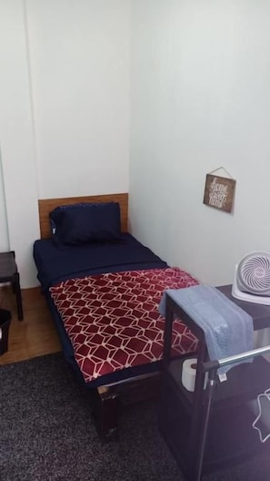 A single bed with a patterned bedspread, a small bedside table, a wall-mounted fan, and a motivational quote sign. - Rooms del Bosque Studios (MORELIA)